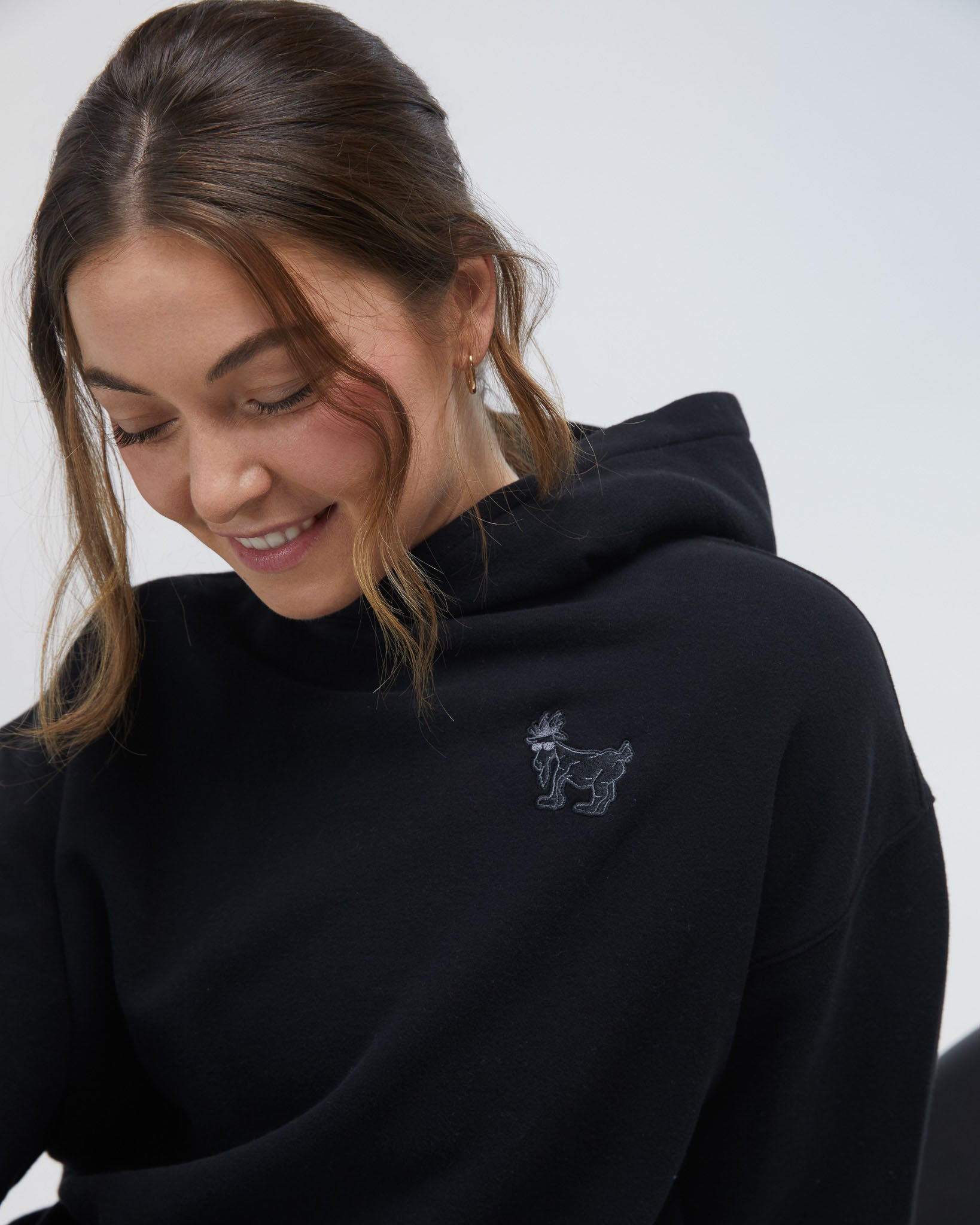 Person wearing a black hoodie with a small embroidered design on a plain background#color_black