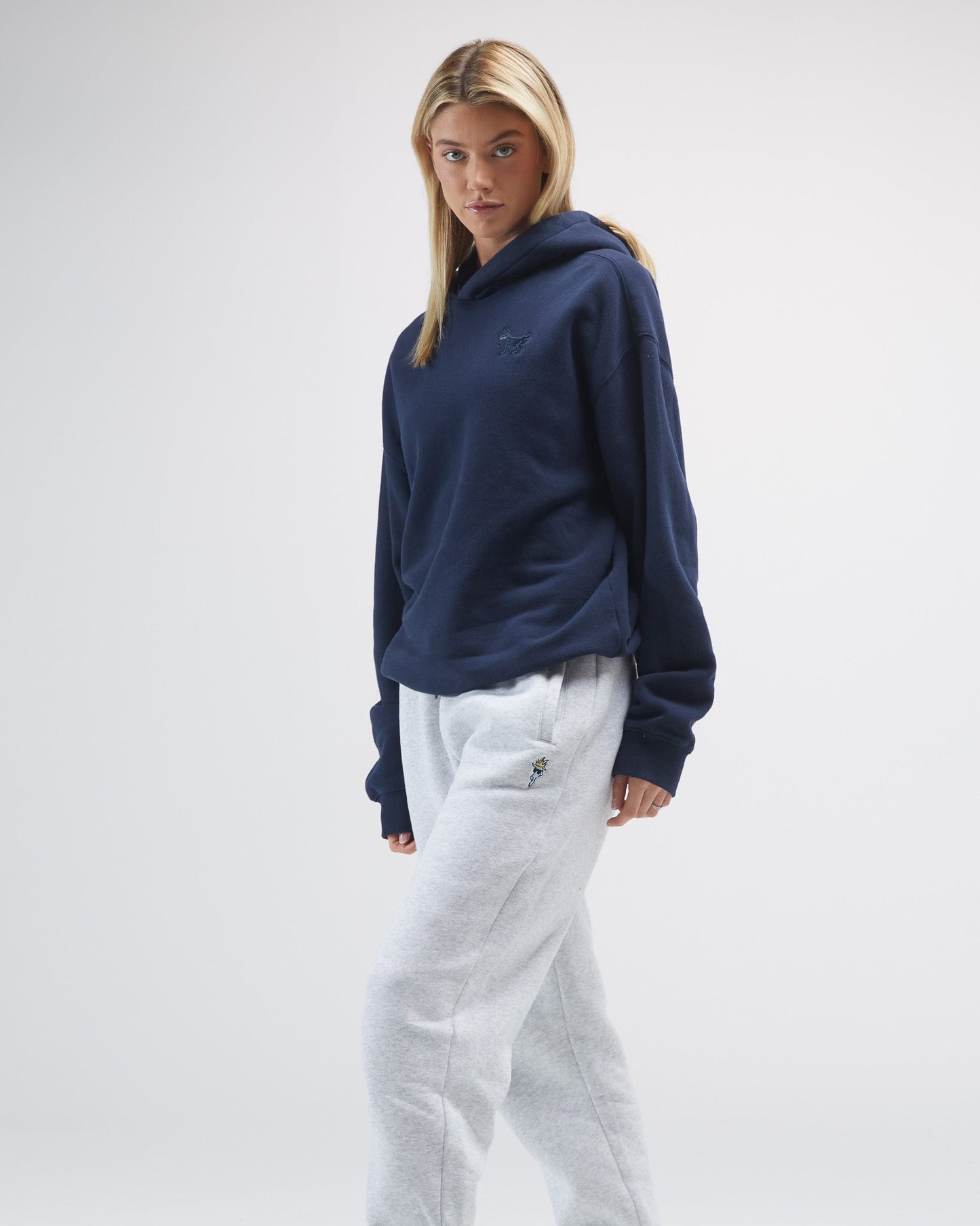 Person wearing a navy hoodie and light-colored pants on a plain background#color_navy-blazer