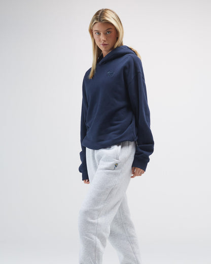 Person wearing a navy hoodie and light-colored pants on a plain background#color_navy-blazer