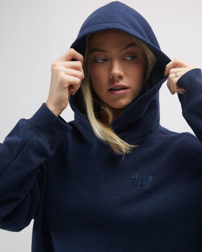 Person wearing a navy blue hoodie with a brand logo on a light gray background#color_navy-blazer