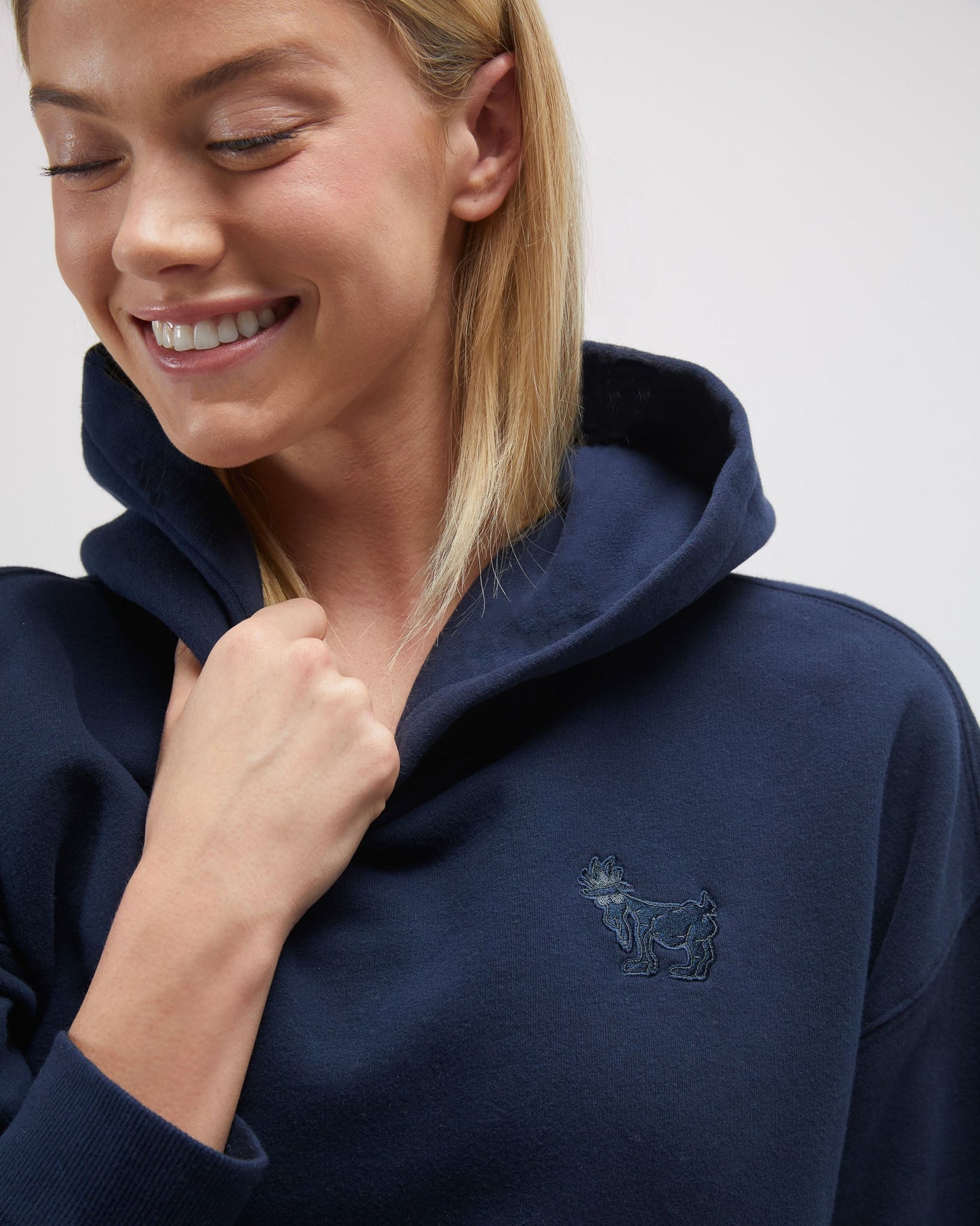 Woman wearing a navy hoodie with a small logo on a plain background#color_navy-blazer