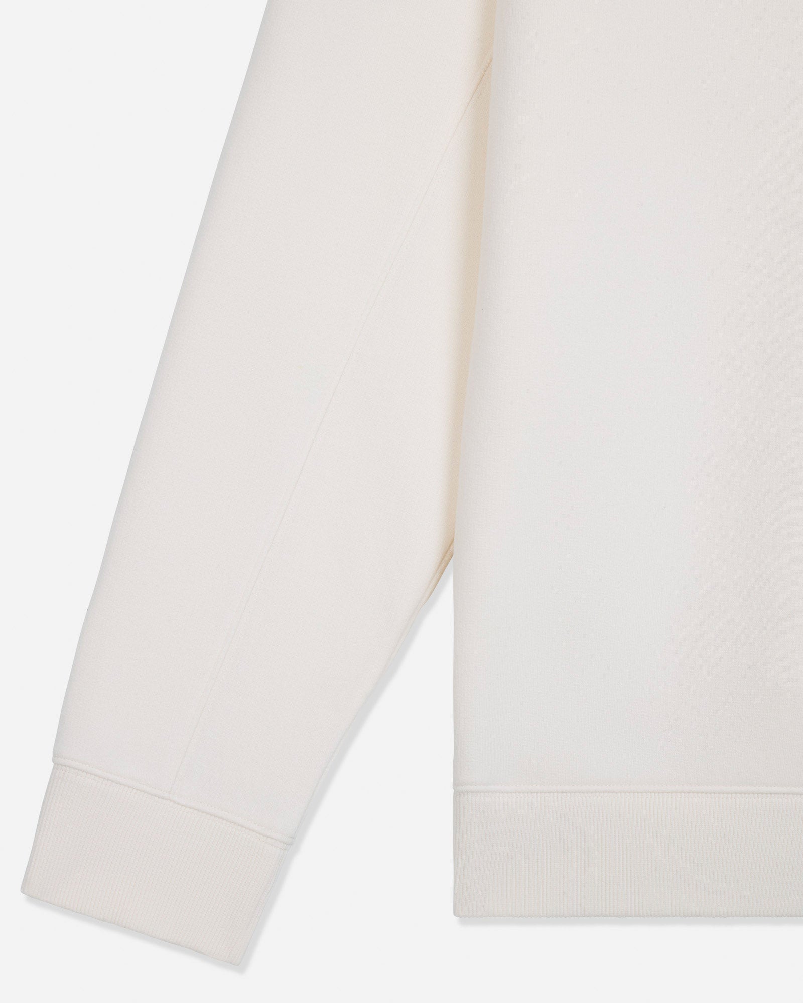 Close-up of a light cream or off-white fabric garment, showing part of a sleeve and the hem with ribbed cuffs and hem.#color_bone