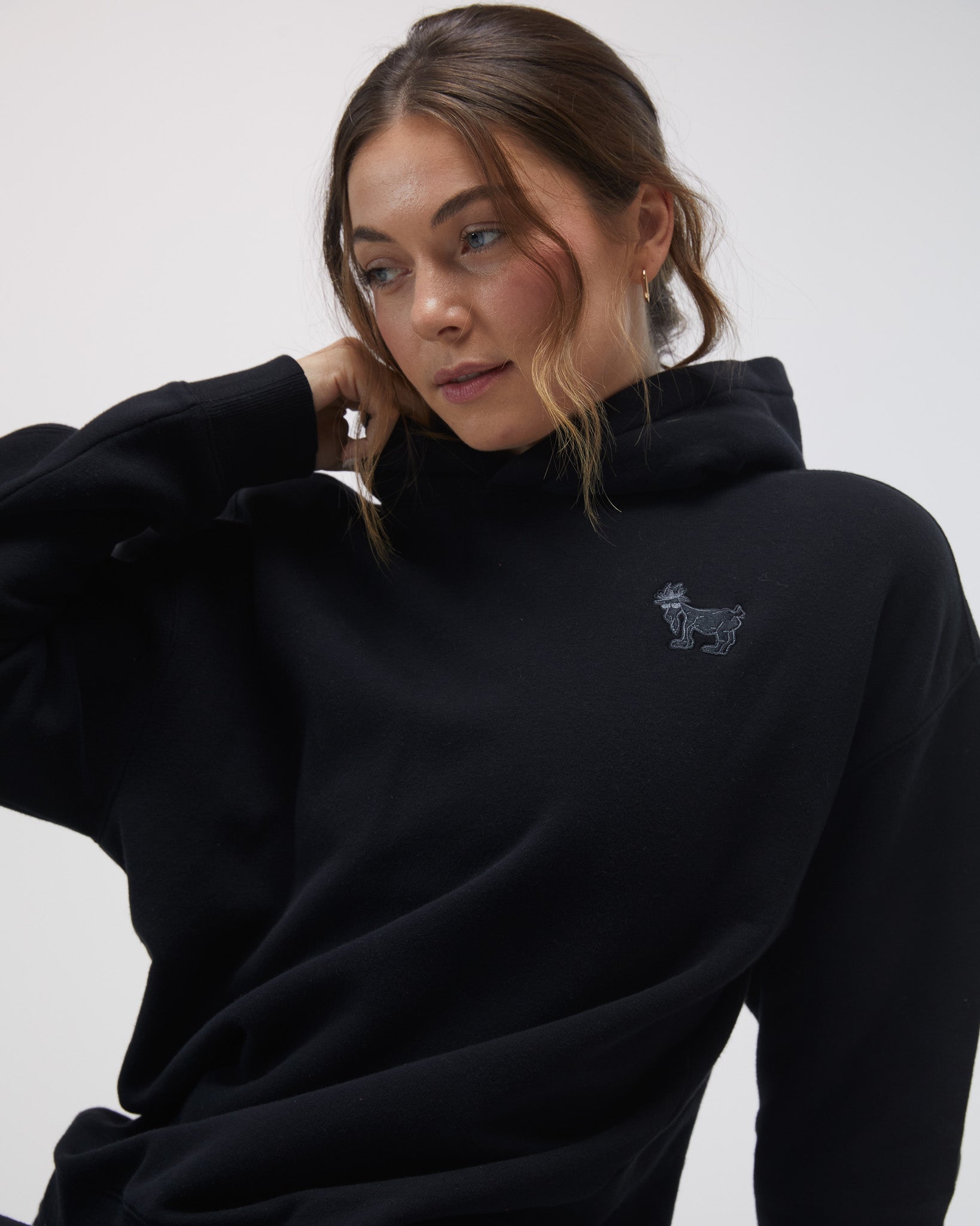 Person wearing a black hoodie with a small logo on a white background#color_black