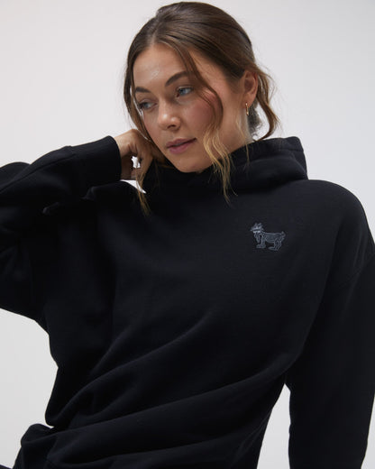 Person wearing a black hoodie with a small logo on a white background#color_black