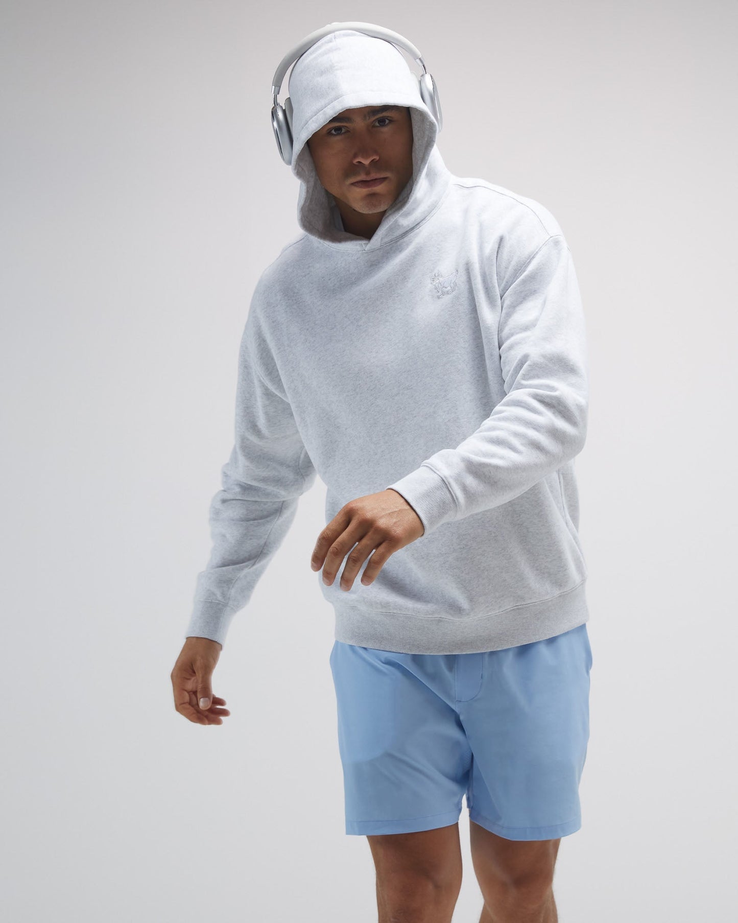 Person wearing a light gray hoodie and blue shorts on a plain background#color_pale-gray