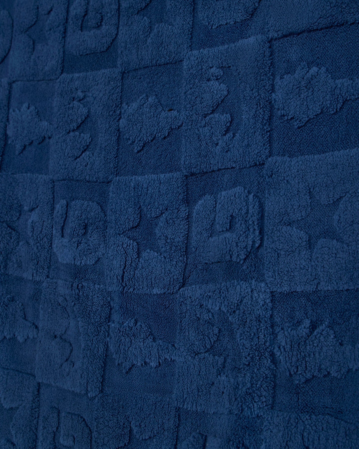 A close-up of a dark navy blue textured fabric with a repeating embossed block pattern.