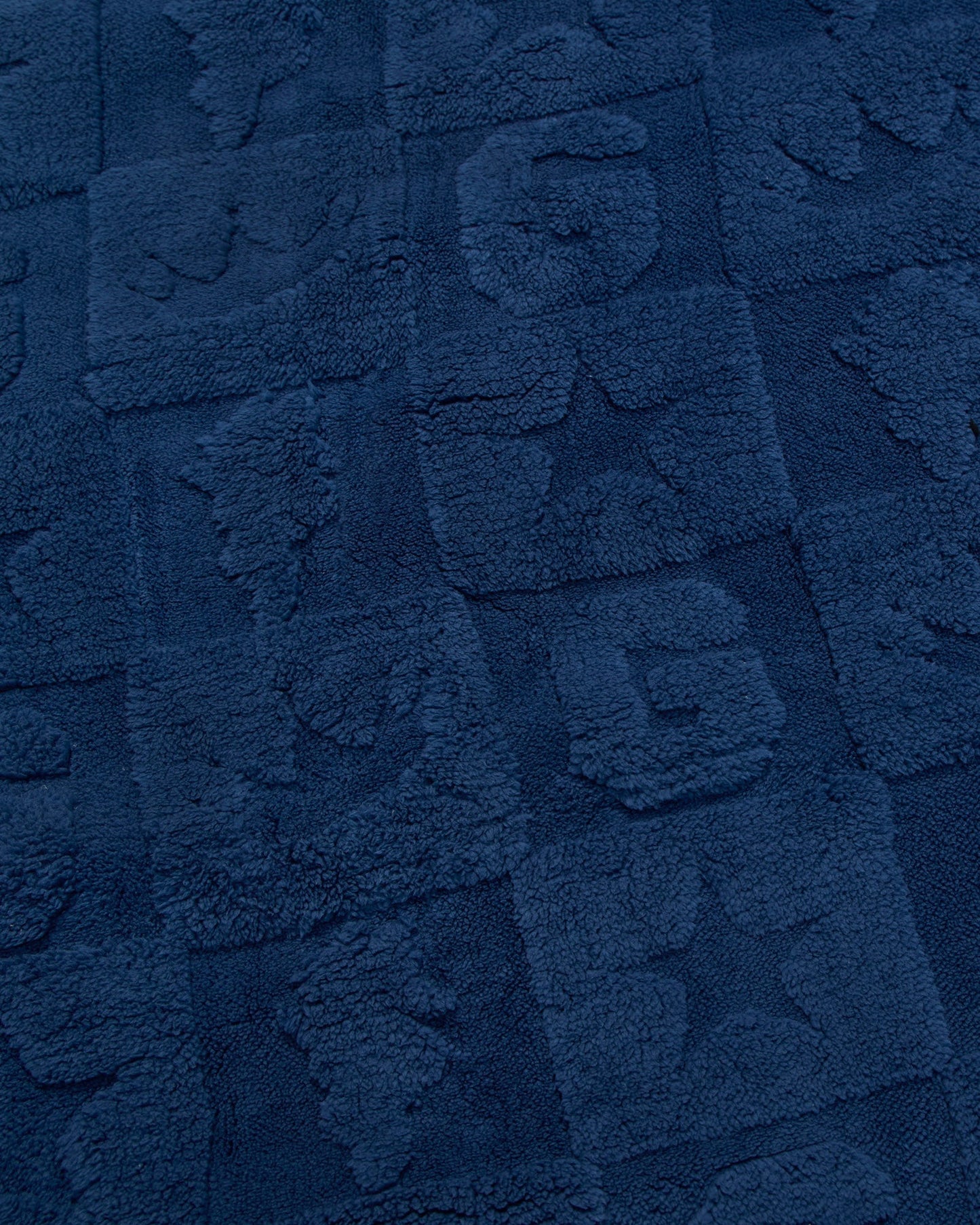 A close-up of a dark navy blue textured fabric with raised block patterns and tufted lettering.