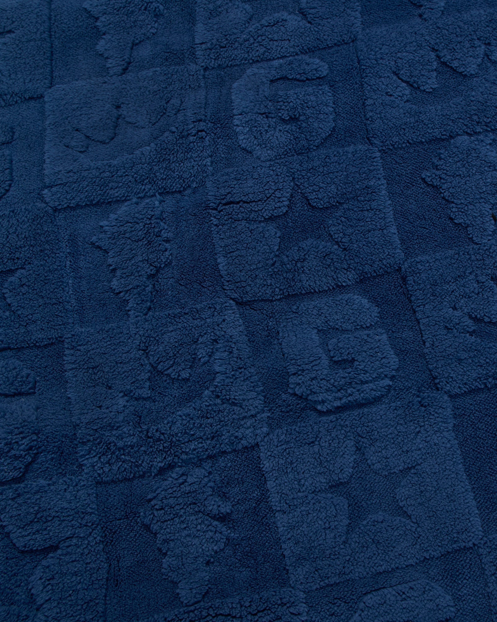 A close-up of a dark navy blue textured fabric with raised block patterns and tufted lettering.