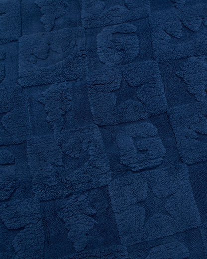 A close-up of a dark navy blue textured fabric with raised block patterns and tufted lettering.