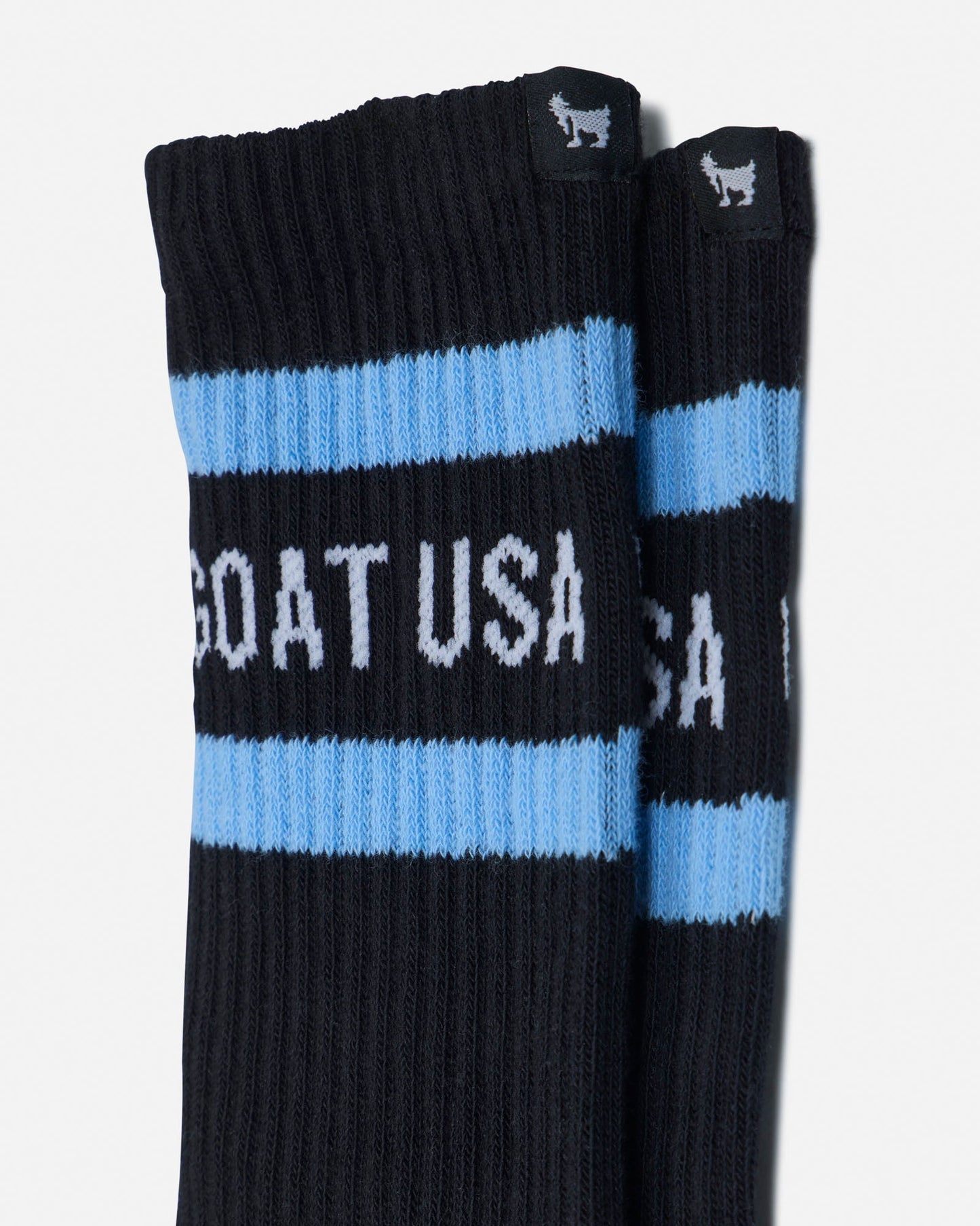 Black socks with blue stripes and 'GOAT USA' text on a light gray background