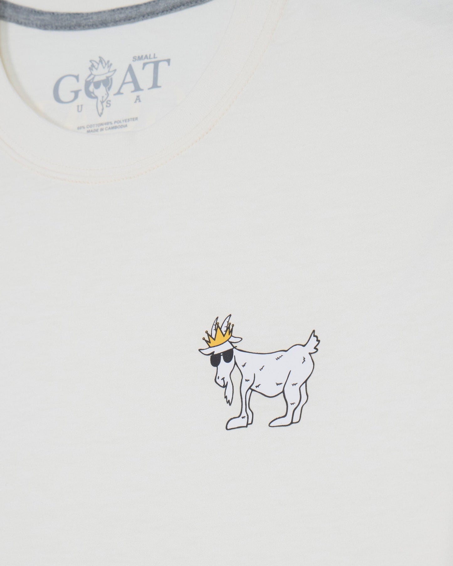 Close-up of a white t-shirt showing the inner neck label with 'GOAT' branding and a small graphic of a goat wearing sunglasses and a crown printed on the chest.#color_bone