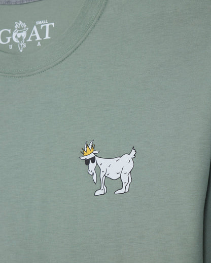 Close-up of a sage green t-shirt featuring a white cartoon goat wearing a gold crown on the chest, with the white 'GOAT' brand logo printed inside the collar.#color_steeped-sage