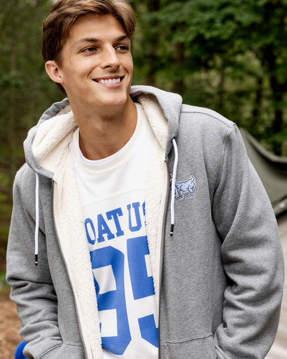 Person wearing a gray hoodie with a white fleece lining and a blue and white graphic t-shirt outdoors.#color_gray