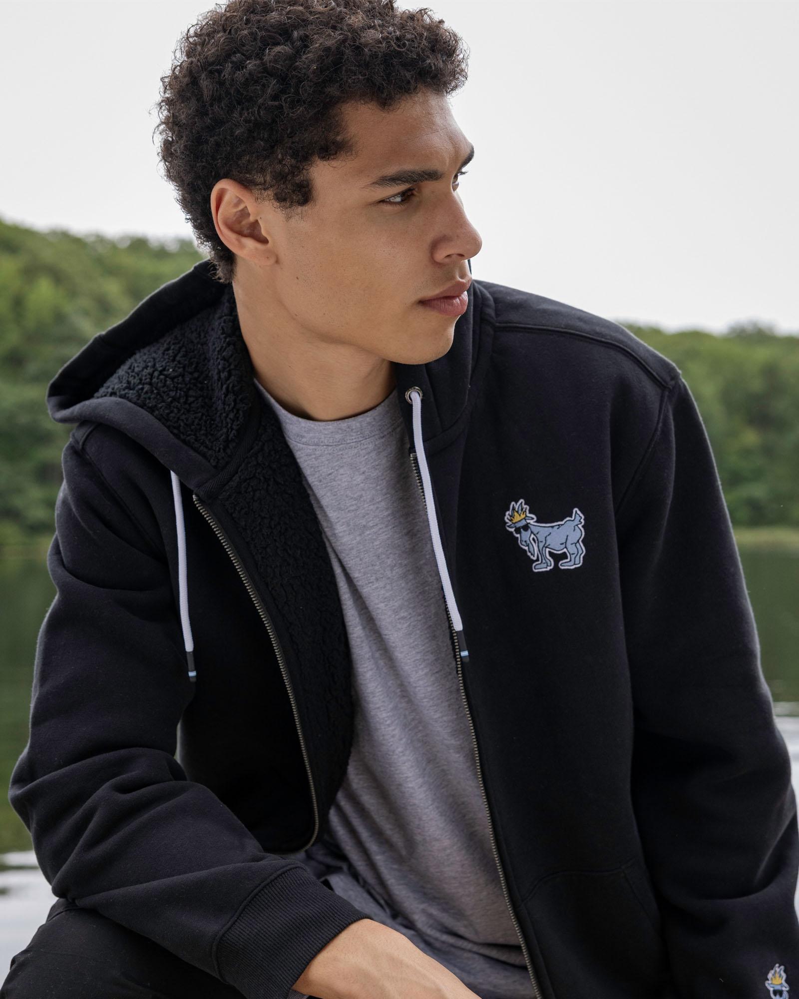 Person wearing a black hoodie with a small logo, sitting outdoors.#color_black