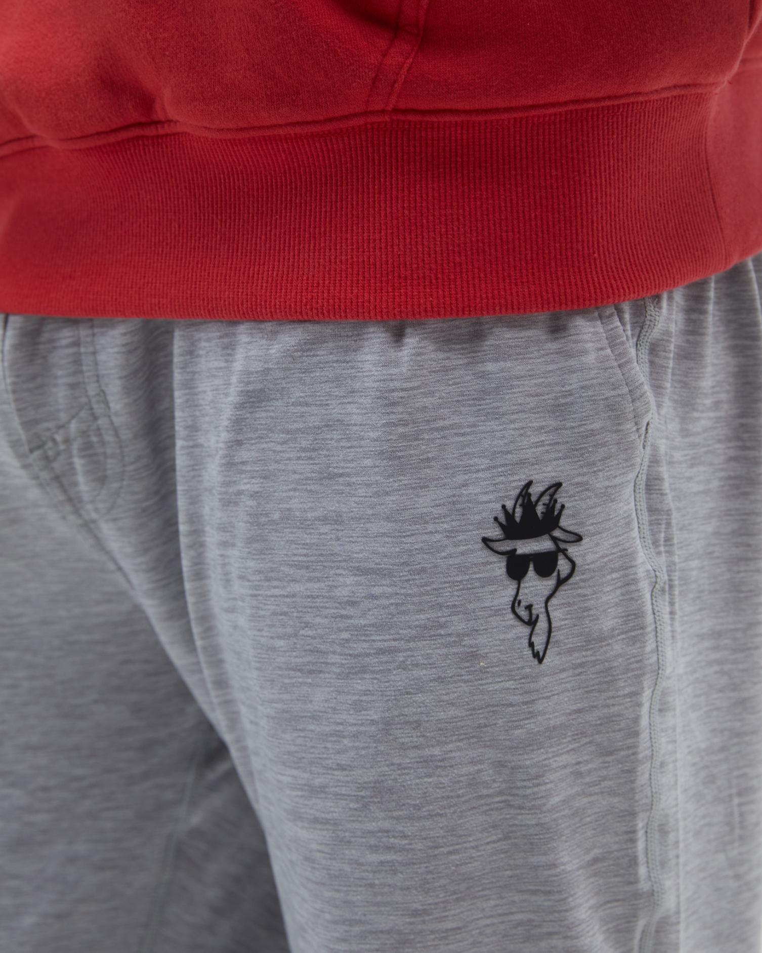 Gray sweatpants with a black embroidered design on the leg, worn with a red hoodie.#color_space-dye-gray