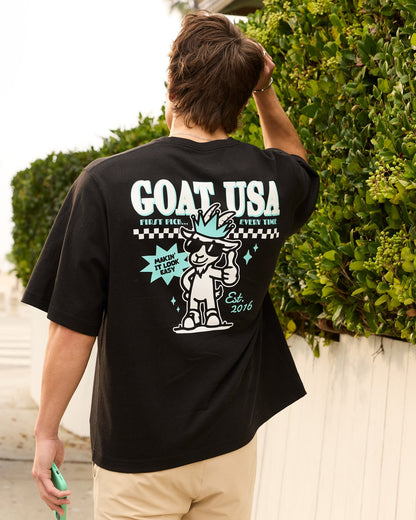 Person wearing a black 'GOAT USA' t-shirt with a graphic design on the back, standing outdoors.