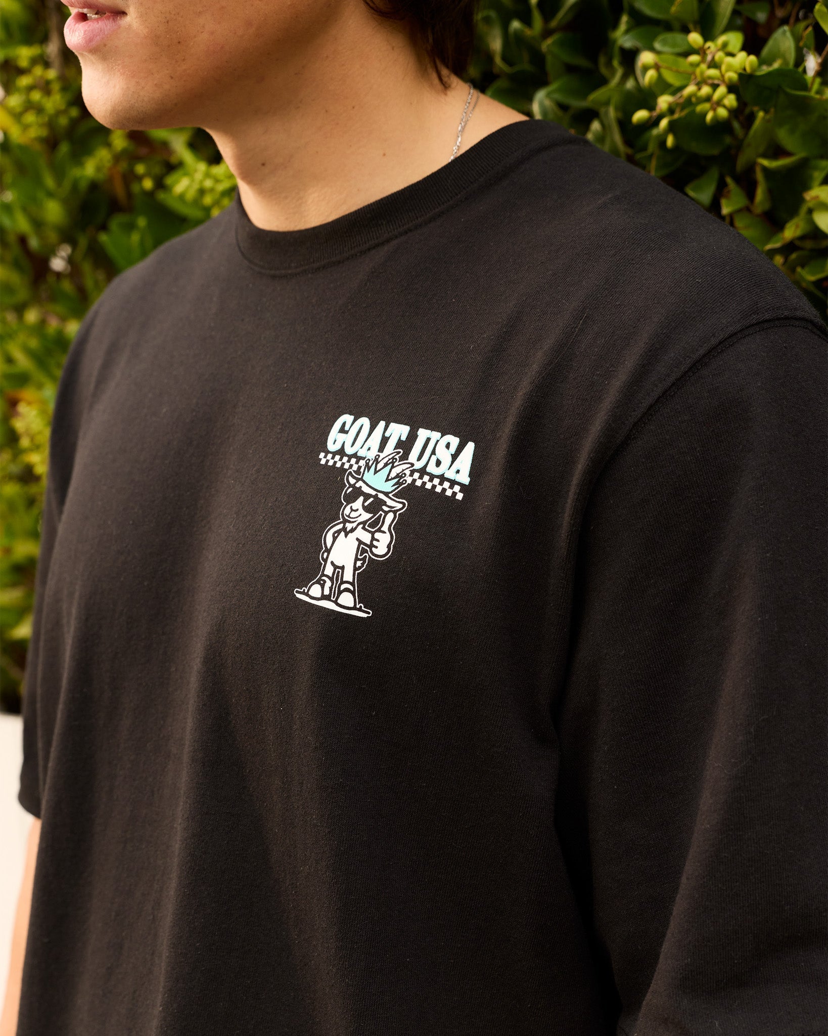 Person wearing a black t-shirt with a graphic design in front of green foliage