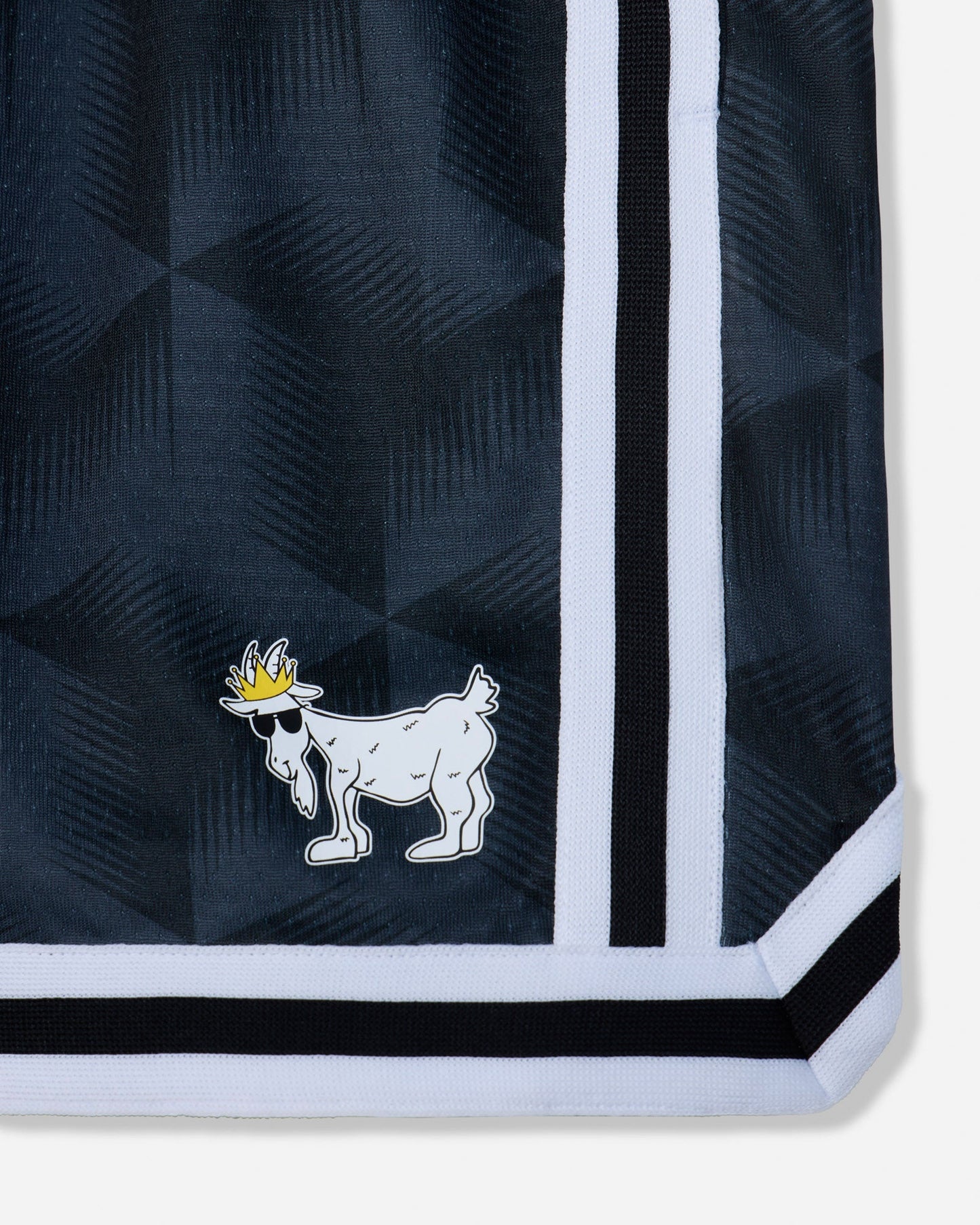 Close-up of a black patterned garment corner with a white and black striped border and a small white goat logo wearing a yellow crown.#color_black