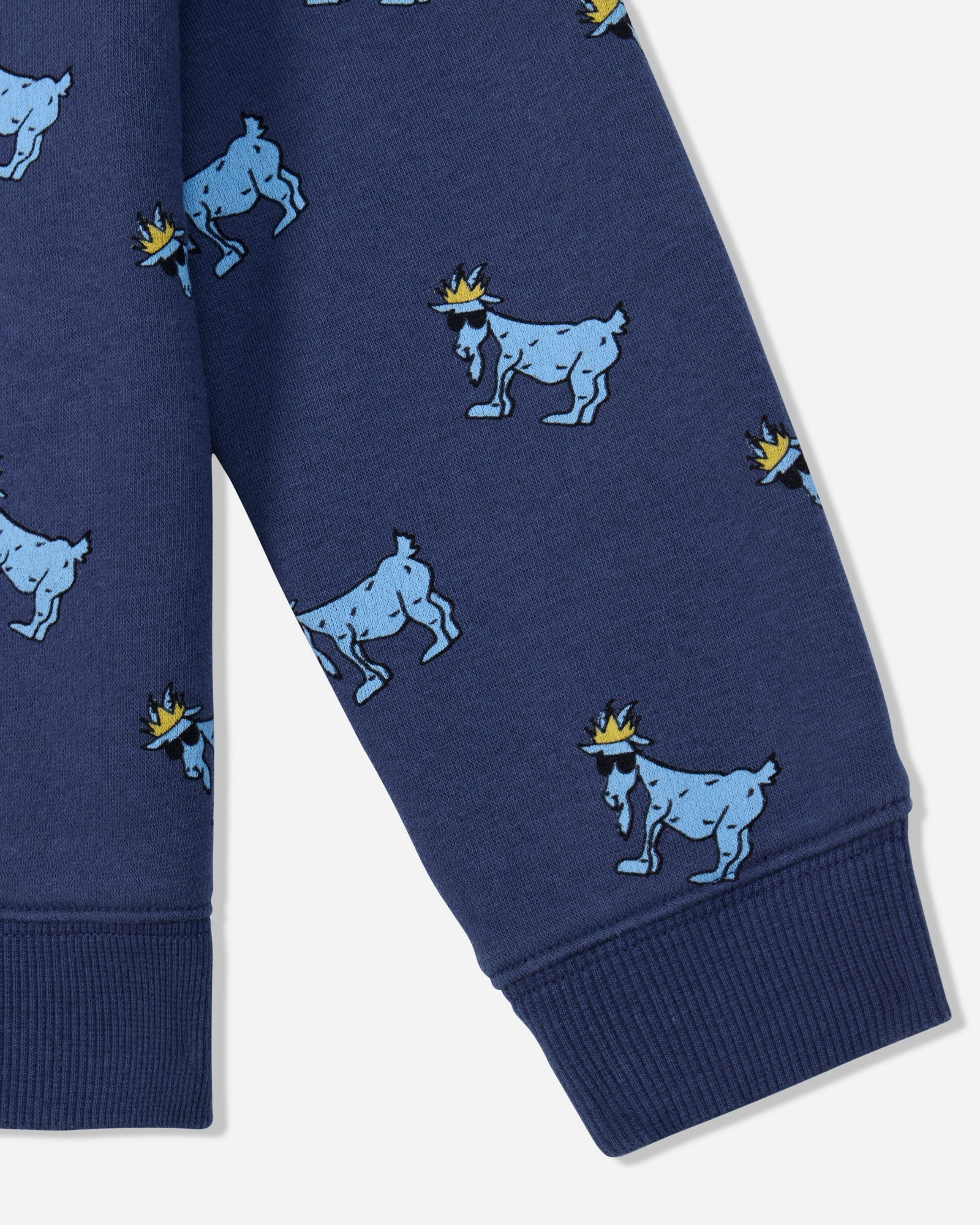 Close-up of a navy blue garment, likely a sweatshirt or pants leg, featuring an allover print of light blue goats wearing small yellow crowns, with ribbed cuffs at the bottom.#color_navy