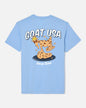 A light blue short-sleeve t-shirt shown from the back, featuring a cartoon graphic of a goat wearing a crown and standing on chocolate chip cookies, with the text 'GOAT USA' and 'Sweet Bites'.