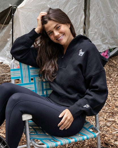 Person wearing a black hoodie with a logo, sitting on chair.#color_black