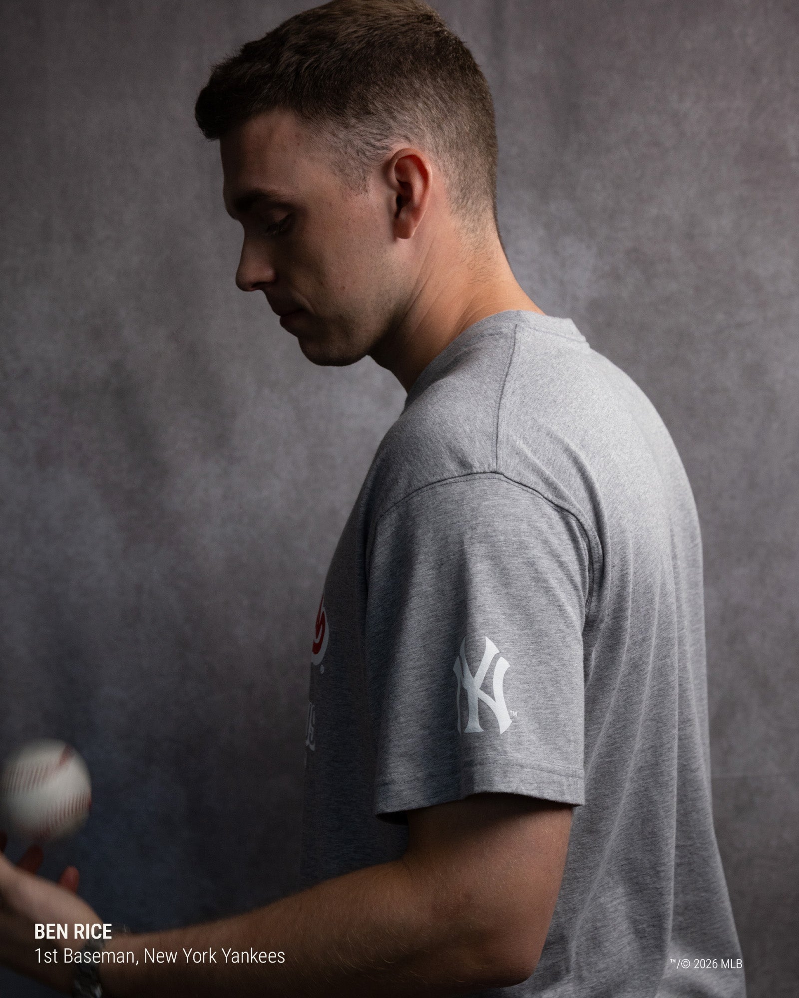 A man in profile wearing a heather gray short-sleeve T-shirt with a white New York Yankees logo on the sleeve, photographed against a textured gray studio background. Text at the bottom left reads 'BEN RICE, 1st Baseman, New York Yankees.
