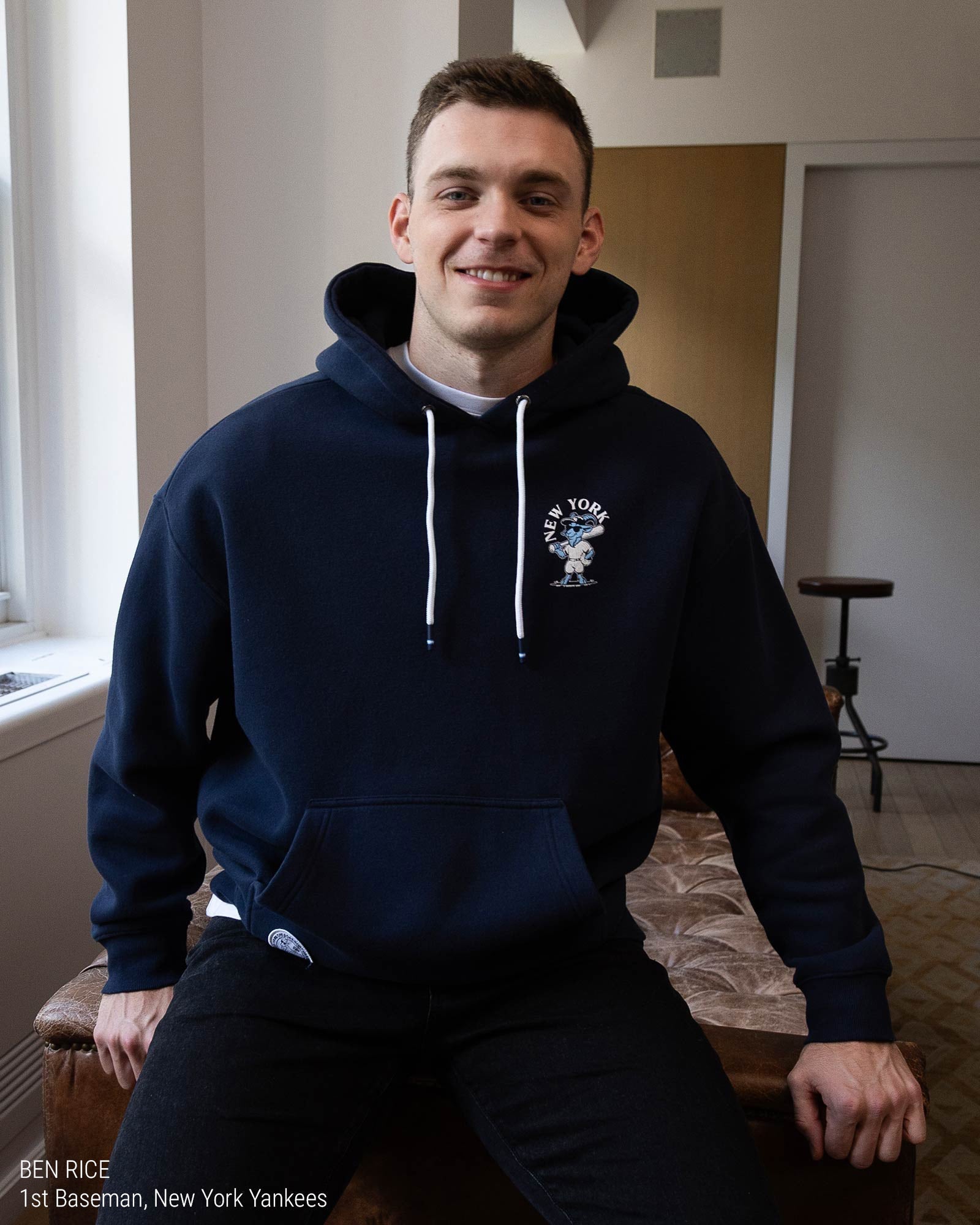 Ben Rice in a navy blue hoodie shown from the back, featuring a white graphic print of the New York Yankees logo with the word 'YANKEES' and a goat illustration on a light gray background.#color_navy