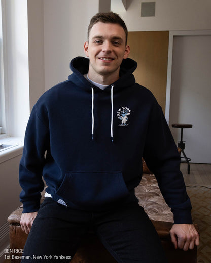 Ben Rice in a navy blue hoodie shown from the back, featuring a white graphic print of the New York Yankees logo with the word 'YANKEES' and a goat illustration on a light gray background.#color_navy