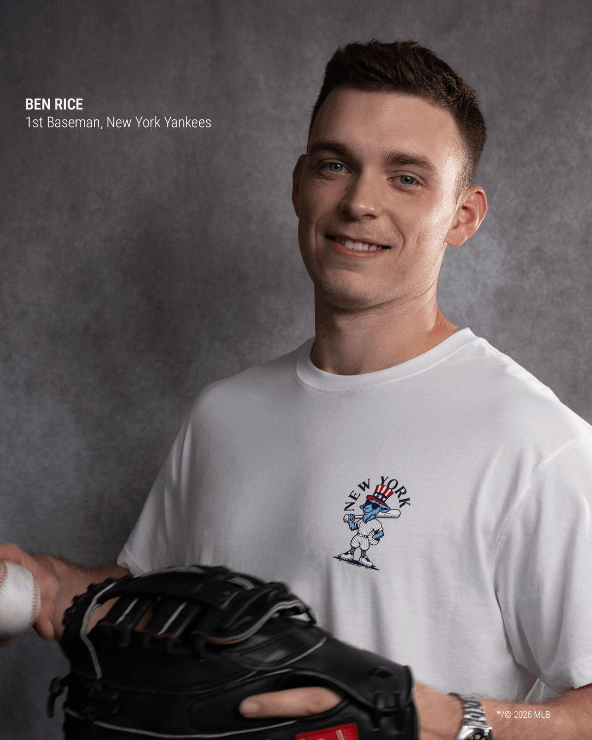 A smiling man in a white New York Yankees graphic t-shirt holds a black baseball glove. The photo has a gray textured studio background, with text in the upper left identifying him as Ben Rice, 1st Baseman, New York Yankees.#color_white