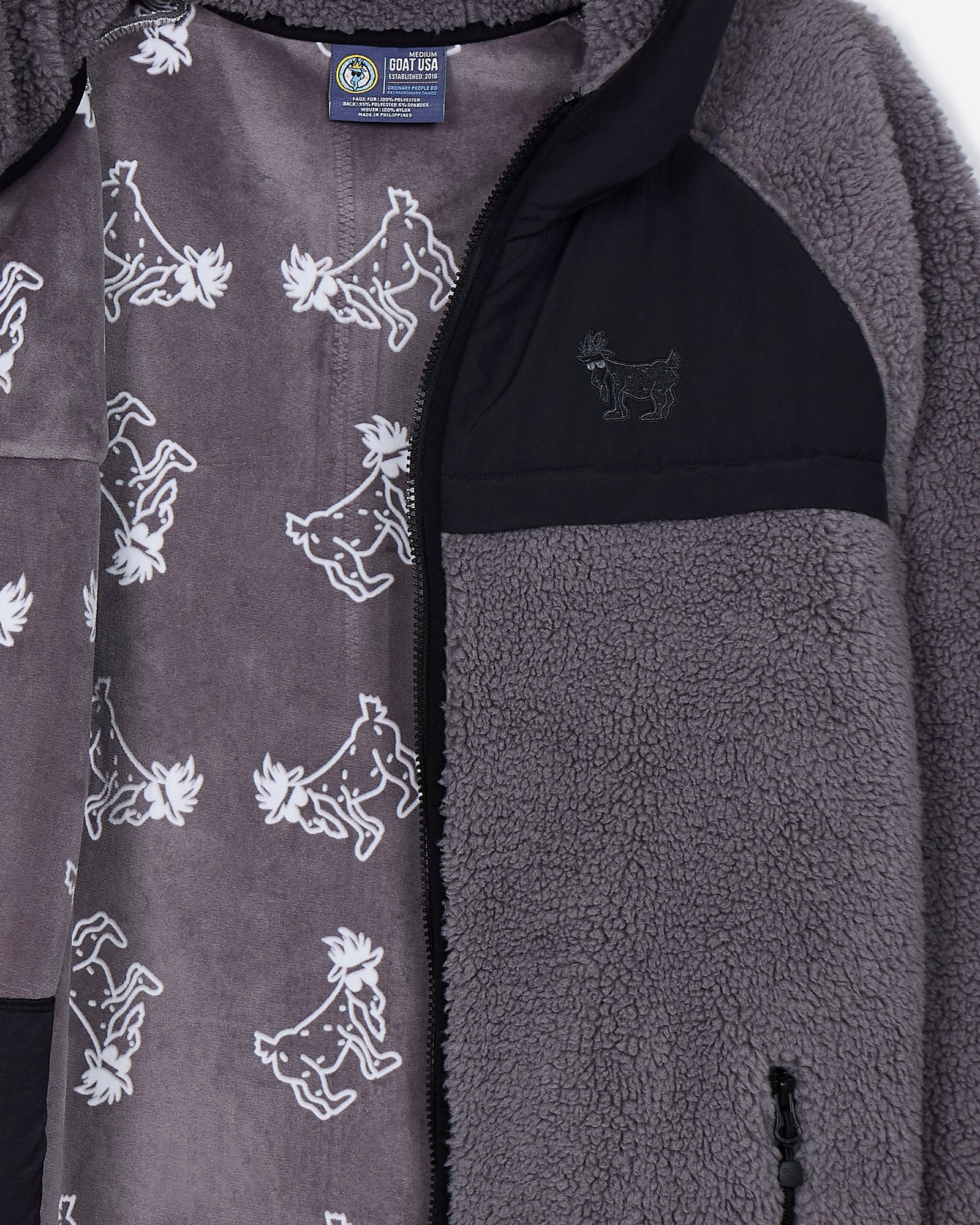 Close-up of a gray fleece jacket with goat pattern and brand label.#color_gray