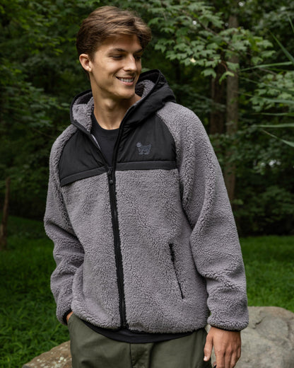 Person wearing a gray and black fleece jacket outdoors with greenery in the background#color_gray