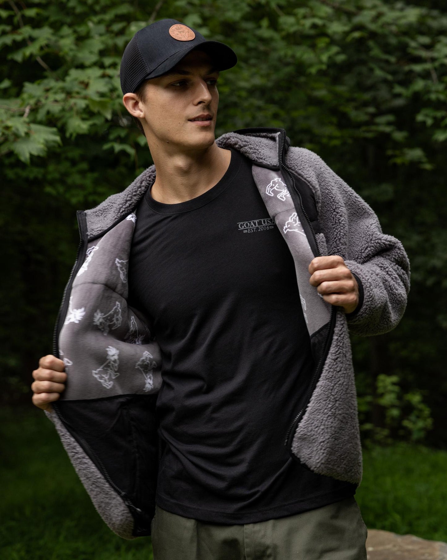 Man wearing a black cap and gray fleece jacket with a forest background#color_gray